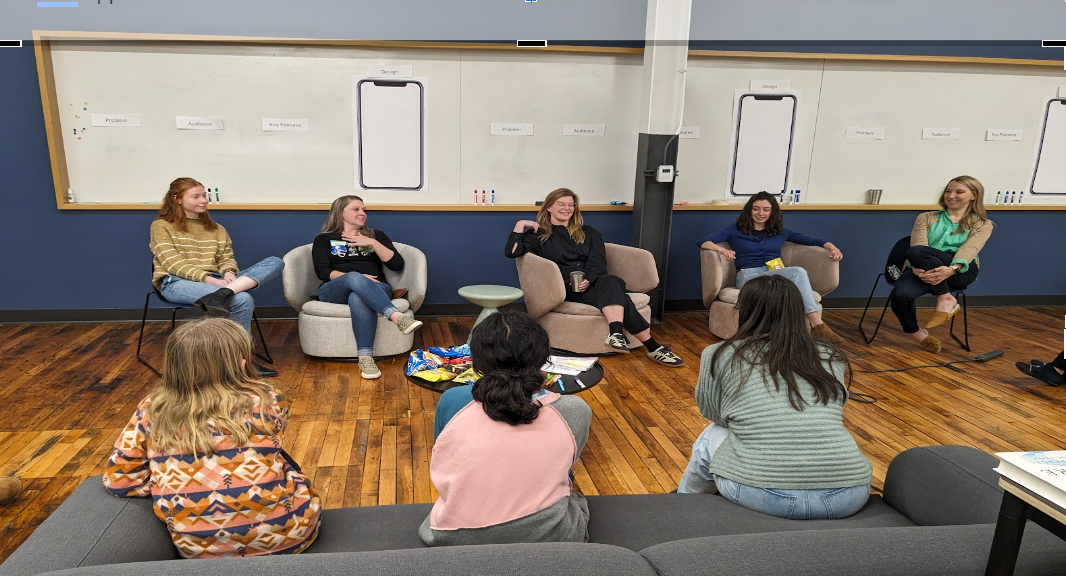 adult women sitting in comfy chairs speaking to young girls on a couch about technology